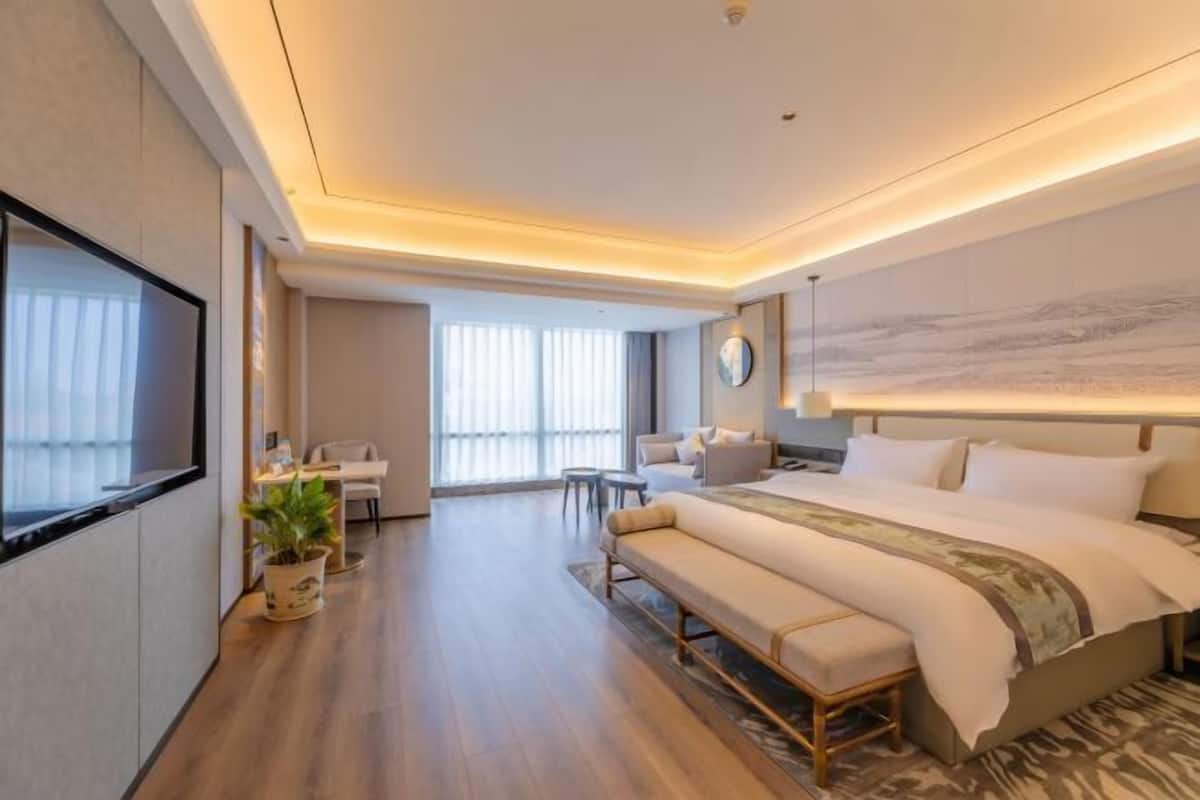 A modern hotel room with a large bed, a desk, a chair, and a television.