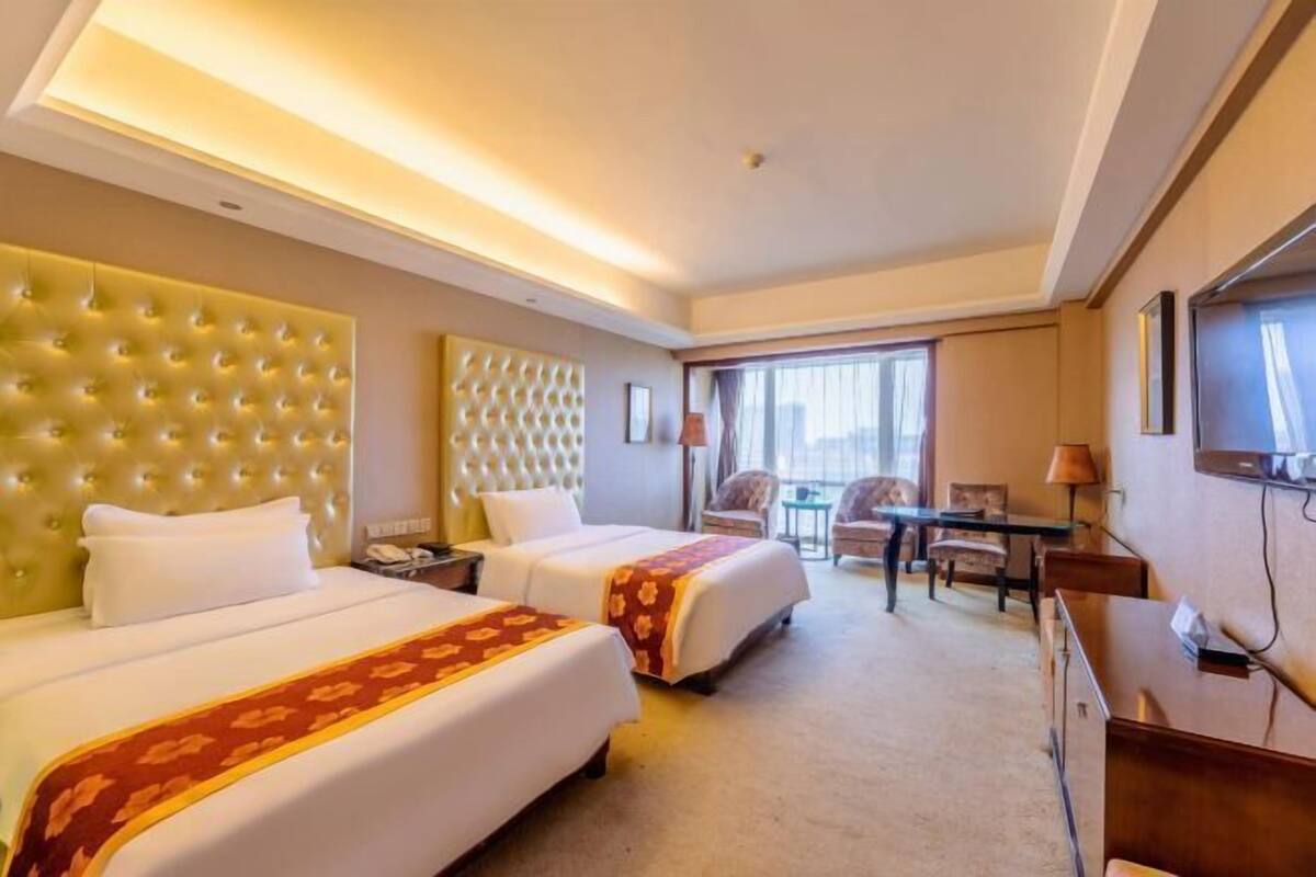 A hotel room with two beds, a desk, a chair, and a television.