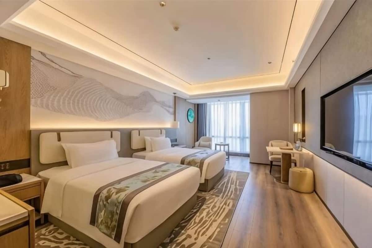 A hotel room with two beds, a desk, a chair, a TV, and a large window.