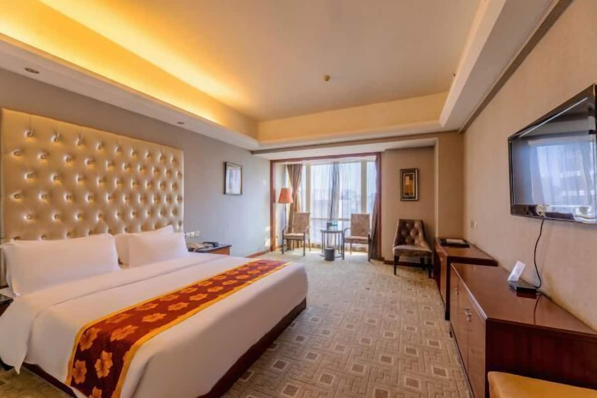 A hotel room with a large bed, a television, a desk, and a seating area with chairs.
