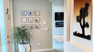 Een moderne hal met een potplant, ingelijste foto’s aan de muur en een schilderij van een cactus.