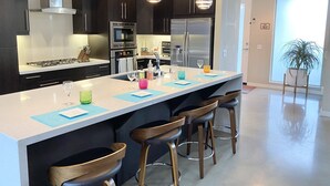 Een moderne keuken met donkere kastjes, roestvrijstalen apparatuur en een centraal eiland met barstoelen.