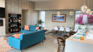 Een moderne woonkamer met een blauwe bank, een eethoek met een glazen tafel en een keukenbar.