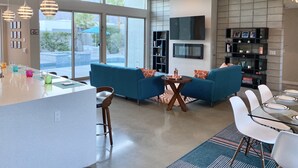 Een moderne woonkamer met een bank, salontafel en een eethoek. Er is een televisie aan de muur bevestigd en een plafondventilator.