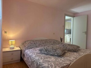 A bedroom with a bed, bedside lamp, and a door leading to a kitchen. - Holiday apartment with pool & balcony (Jadranovo)