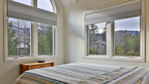 A bedroom with a large bed, two windows, a nightstand, and a view of trees and mountains. - Beautiful Fall Line Condo with Mountain Views on Shuttle Route B4A/B (Killington)