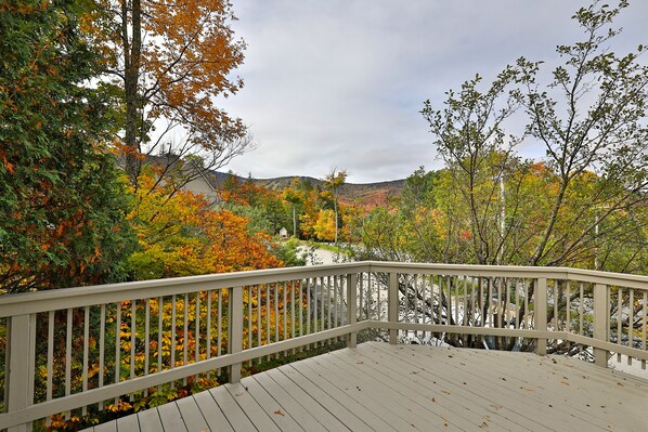 A wooden deck with a railing overlooking a forested area with autumn foliage.