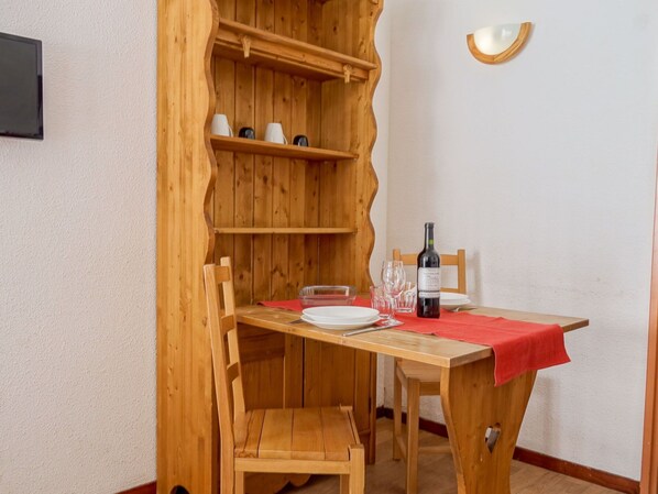 Et træspisebord med stole, en vinflaske og glas på en rød dug.