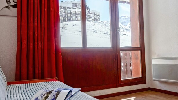 A room with a bed, a window with a view of a building and mountains, and a red curtain. - Lovely apartment for 2 people with WIFI (Les Boisses)