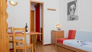 A room with a wooden dining table and chairs, a bed with striped bedding, a small bedside table with a lamp, and a wall-mounted picture. - Lovely apartment for 2 people with WIFI (Les Boisses)