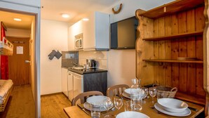 A compact kitchen with a microwave, sink, and stove, a dining table set with plates and glasses, and a TV mounted on the wall. - Lovely apartment for 4 people with WIFI, TV, balcony and panoramic view (Les Boisses)