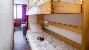 A bunk bed room with a wooden headboard, a window with curtains, and a door leading to another room. - Lovely apartment for 4 people with WIFI, TV, balcony and panoramic view (Les Boisses)