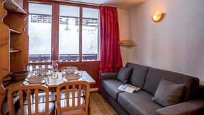 A cozy room with a dining table set for four, a grey sofa, and a window with a view of a snowy landscape. - Lovely apartment for 4 people with WIFI, TV, balcony and panoramic view (Les Boisses)