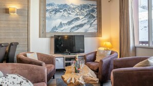 Una sala de estar acogedora con sofás de cuero, una mesa de centro de madera, un televisor de pantalla plana y un cuadro grande de montañas en la pared.
