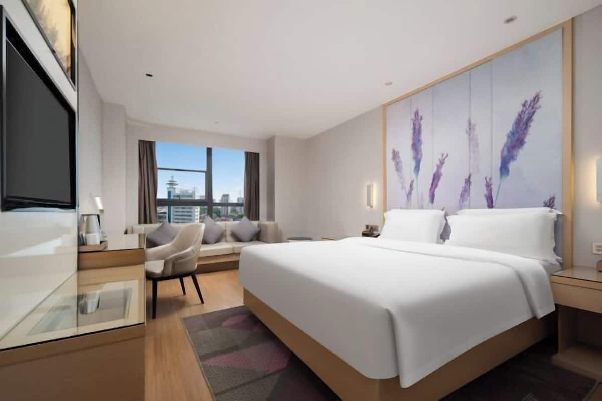 A modern hotel room with a large bed, a seating area with a view of the city, and a flat-screen TV.