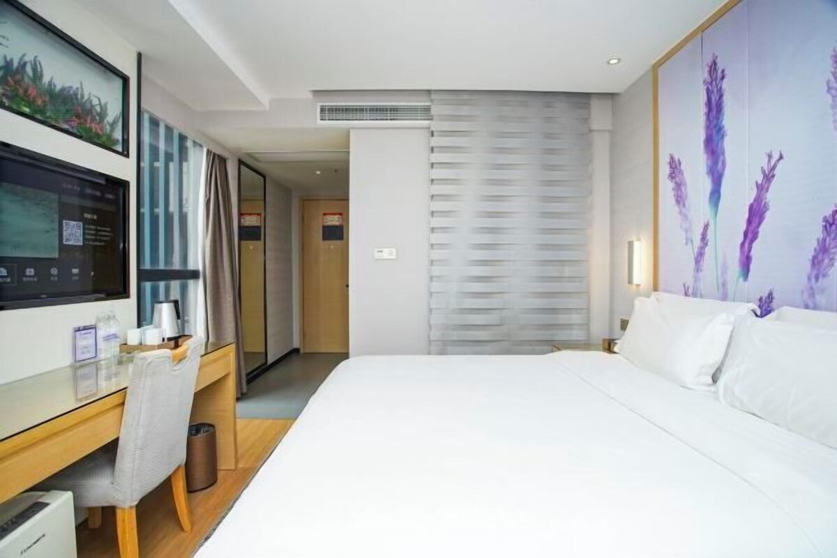 A hotel room with a bed, a desk with a chair, a TV, and a large window.