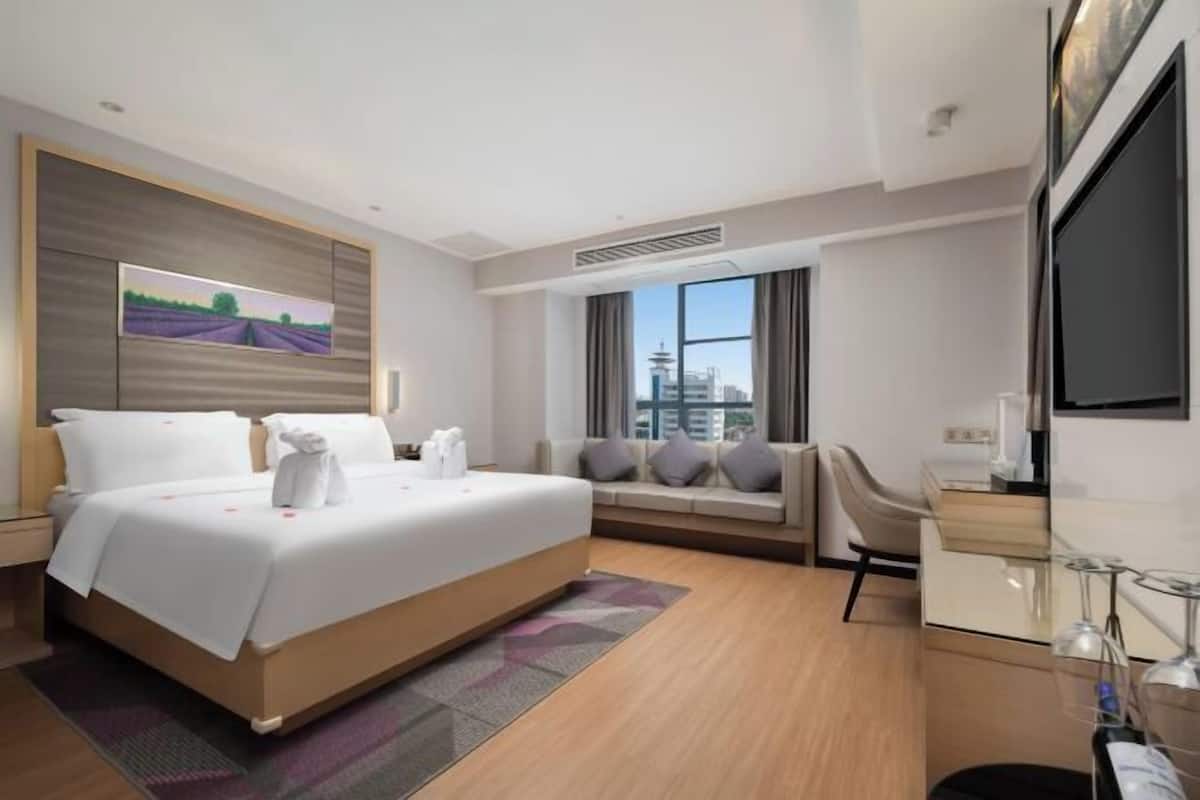 A modern hotel room with a large bed, a sofa, a desk, and a TV.