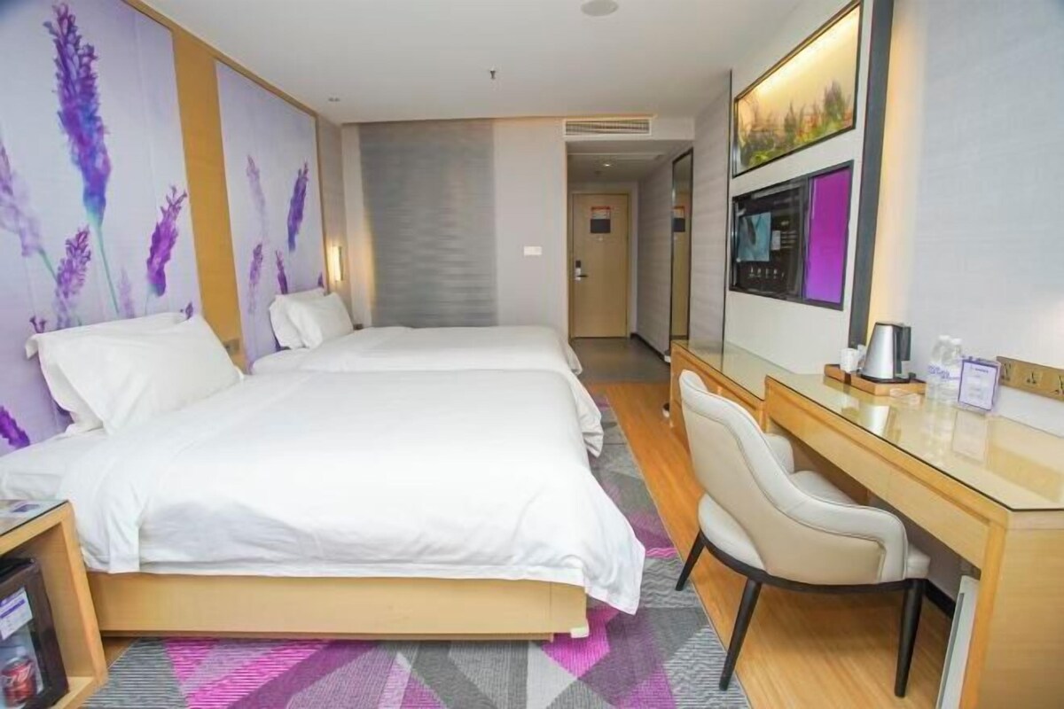 A hotel room with a bed, a desk, and a chair. There is a door leading to another room.