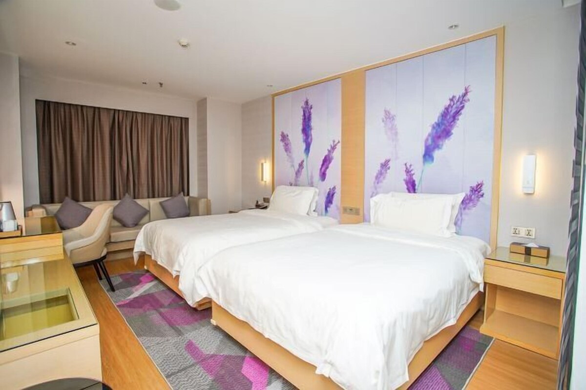 A hotel room with two beds, a sofa, a desk, and a large window with curtains.