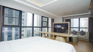 Una habitación de hotel moderna con una cama grande, un televisor sobre un soporte de madera y ventanas amplias que ofrecen vistas a la ciudad.