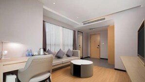 Habitación de hotel moderna con sofá, una mesita redonda, escritorio con silla y un ventanal con cortinas.