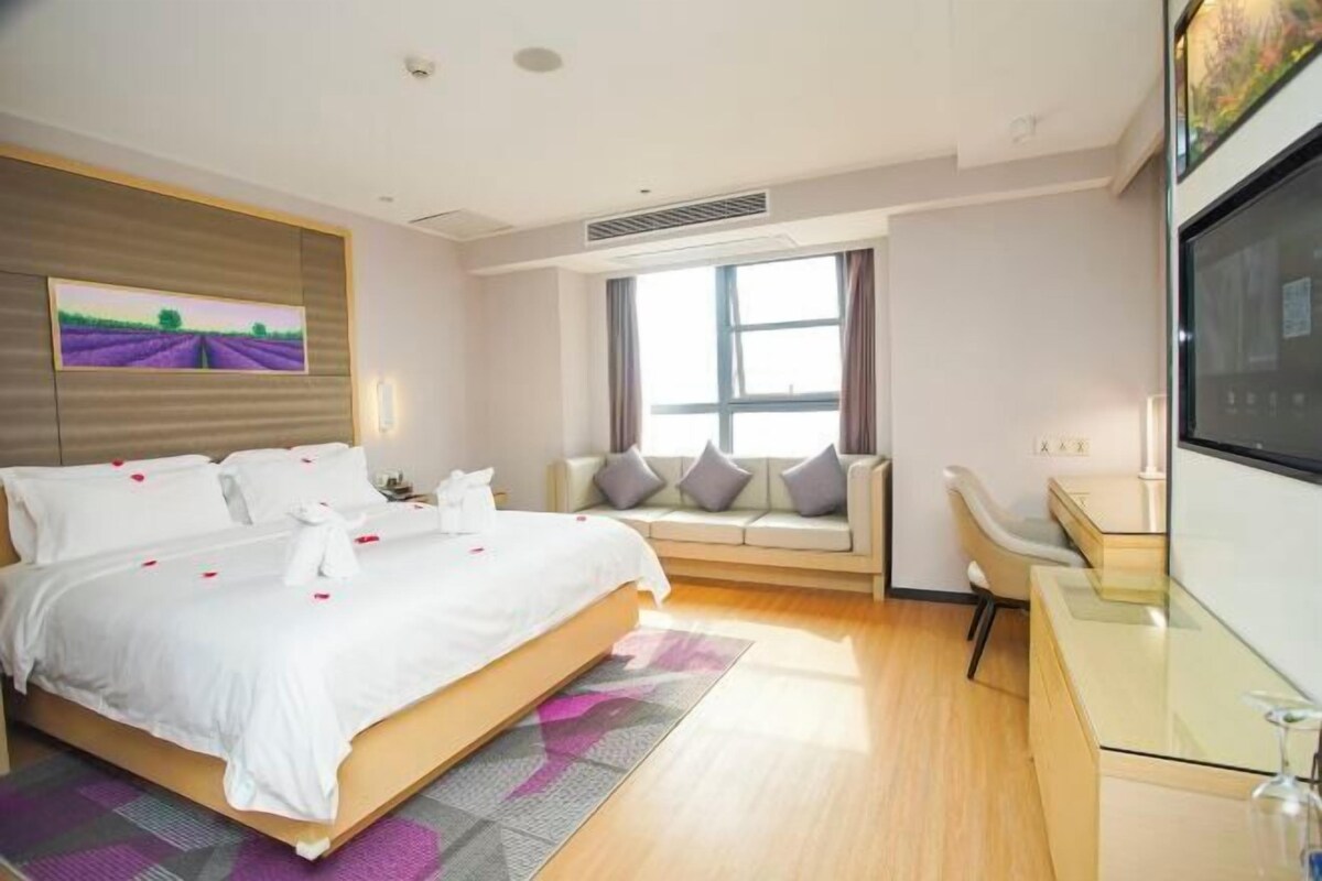 A modern hotel room with a large bed, a sofa, a desk, and a TV.