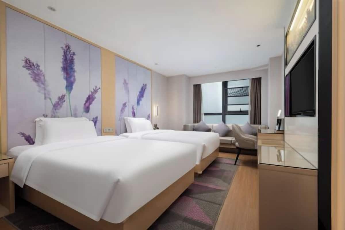 A hotel room with two beds, a sofa, a TV, and a large window.