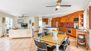 A modern kitchen with wooden cabinets, a blue countertop, and a dining area with a glass table and chairs. - Regatta Noosa - Top Floor Magic Views (Noosaville)
