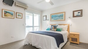 A bedroom with a bed, bedside table, and artwork on the walls. - Regatta Noosa - Top Floor Magic Views (Noosaville)