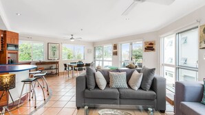 A spacious living area with a grey sofa, dining table, and bar area. - Regatta Noosa - Top Floor Magic Views (Noosaville)