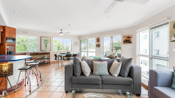 A spacious living area with a grey sofa, dining table, and bar area.