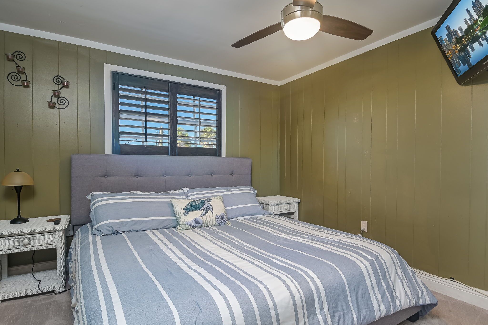 A bedroom with a bed, a nightstand, a lamp, a ceiling fan, and a window with blinds.