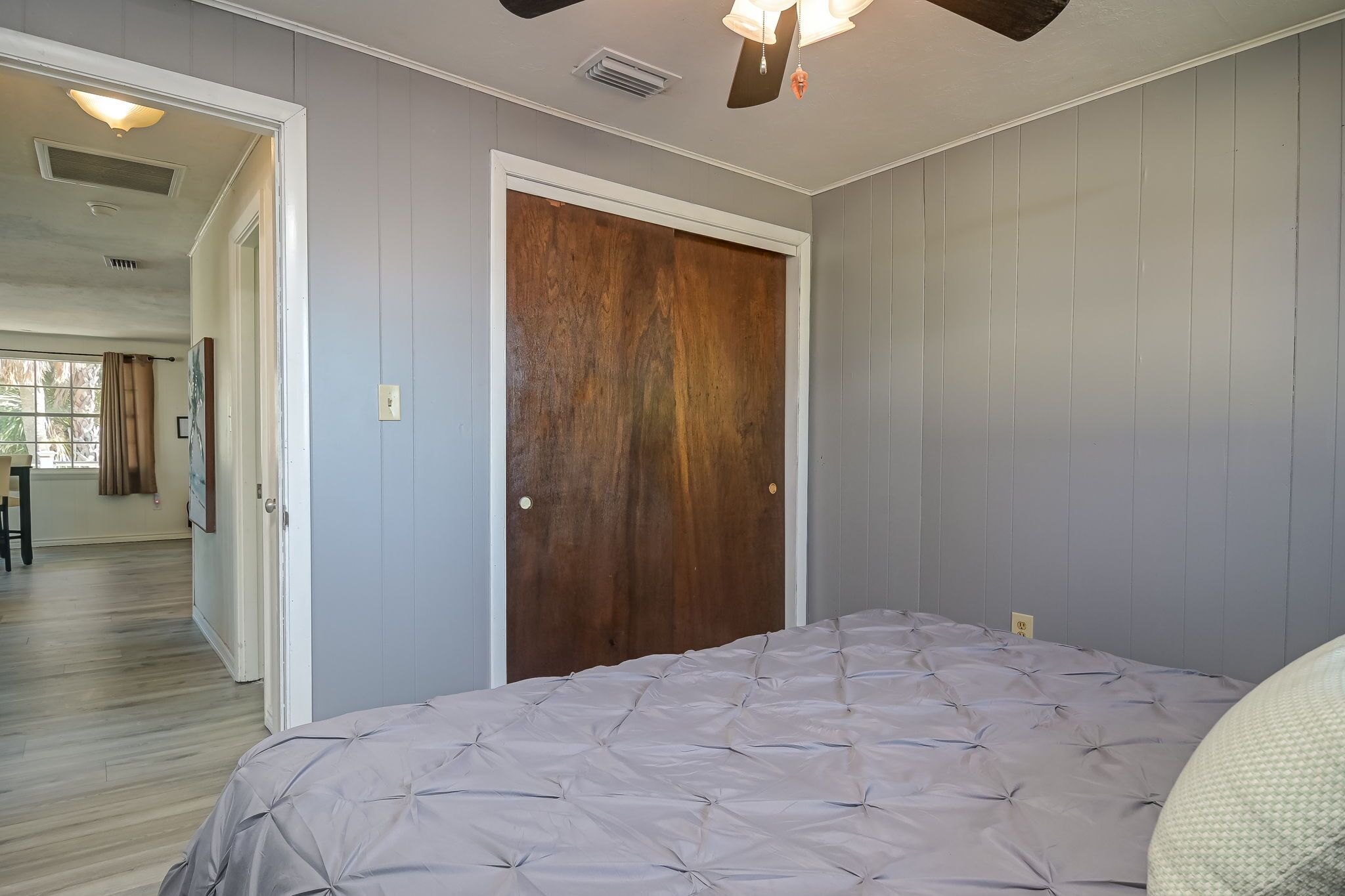A bedroom with a large bed, a wooden door, and a ceiling fan.