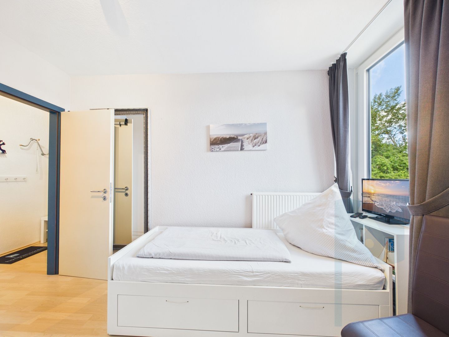 Une chambre à coucher avec un lit, une fenêtre avec des rideaux, un radiateur et un tableau accroché au mur.