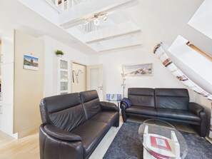 Un salon moderne avec deux canapés en cuir noir, une table basse en verre et un escalier menant à un niveau supérieur.