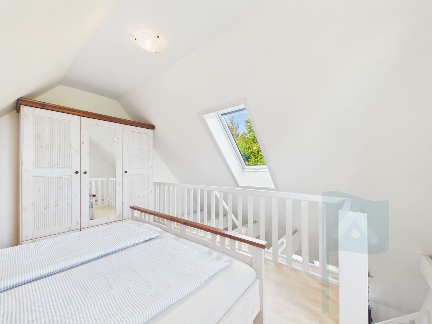 Un dormitorio con techo inclinado, tragaluz, cama con ropa de cama a rayas y un armario blanco.