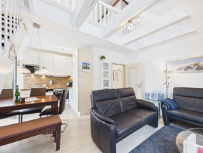 A modern living room with a leather sofa, a dining table with chairs, and a kitchen in the background.