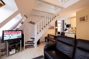 Una sala moderna con una escalera, un televisor de pantalla plana, un sofá de cuero y una zona de comedor.