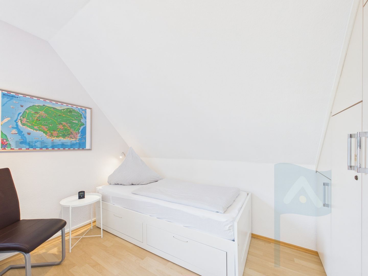 Quarto com uma cama de solteiro, uma mesinha, uma cadeira e um mapa na parede.