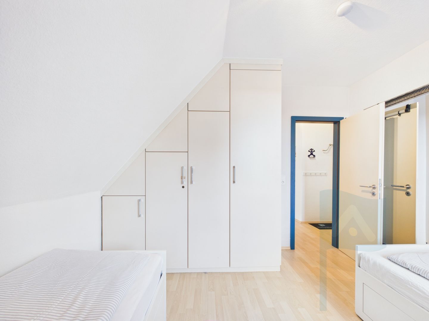 A modern bedroom with a sloped ceiling, a bed, a wardrobe, and a bathroom with a shower.