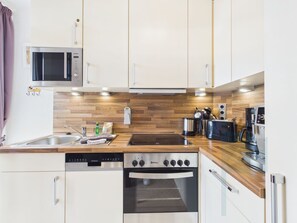 A modern kitchen with white cabinets, a wooden backsplash, a stainless steel sink, a Bosch oven, a Siemens dishwasher, and a microwave.