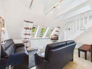 A modern living room with a sofa, a television, and a staircase. - Ferienwohnung Südstrand - Keine 5 Minuten vom Strand Entfernt (Wyk auf Föhr)