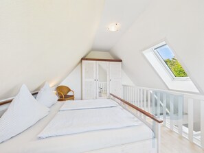 A bedroom with a sloped ceiling, a skylight, a bed with striped bedding, a wicker chair, and a white wardrobe. - Ferienwohnung Südstrand - Keine 5 Minuten vom Strand Entfernt (Wyk auf Föhr)