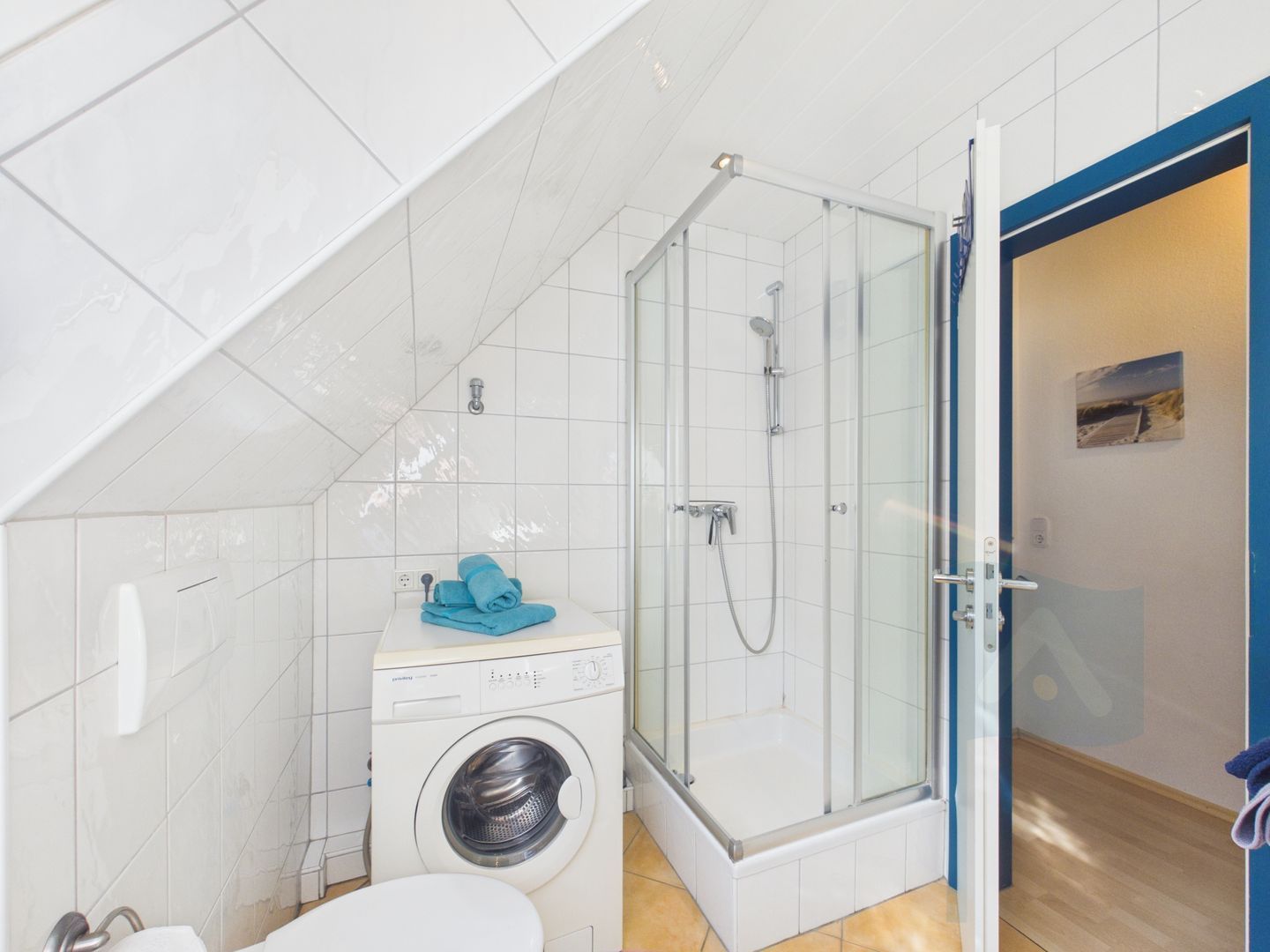 A compact bathroom with a washing machine, a glass-enclosed shower, and a white toilet.