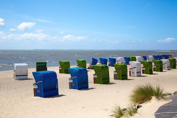 Ein Strand mit Reihen von nummerierten Liegestühlen und einer Reihe weißer Strandhütten.