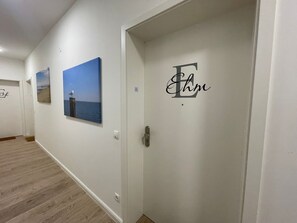 Ein Korridor mit Holzboden, einer Tür mit Monogramm und zwei gerahmten Bildern an der Wand.