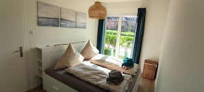A bedroom with a bed, pillows, a hanging light fixture, and a view of greenery outside.