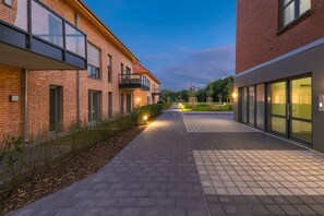 Un sendero entre edificios con fachadas de ladrillo, un camino pavimentado y equipo de ejercicio al aire libre.