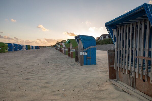 Eine Reihe von Strandhütten mit nummerierten Schildern, ein Sandstrand und ein klarer Himmel.