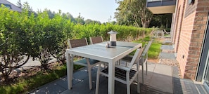 An outdoor patio with a table and chairs, surrounded by greenery and a brick wall.